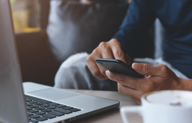 Man using mobile phone whilst sat at a computer