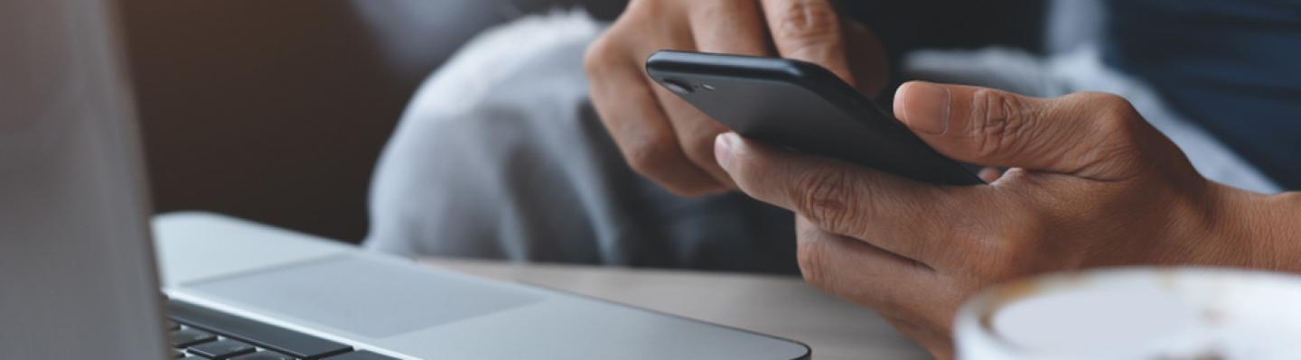 Man using mobile phone whilst sat at a computer